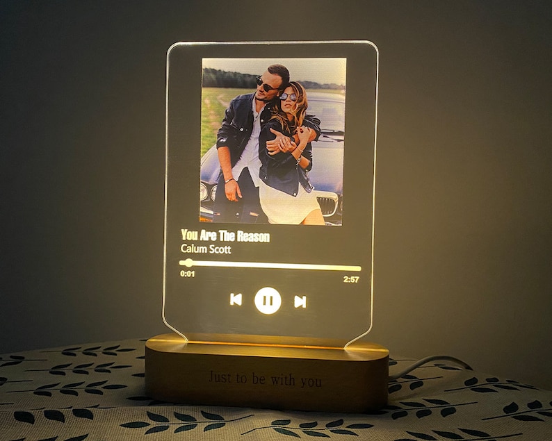 May include: A white and gold acrylic music player with a photo of a couple in a car. The player has a black and white progress bar with the song title "You Are The Reason" by Calum Scott. The base of the player is made of wood and has the text "Just to be with you" engraved on it.