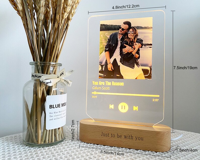 May include: A wooden music player night light with a clear acrylic panel displaying a photo of a couple and the song title "You Are The Reason" by Calum Scott. The base of the night light is engraved with the text "Just to be with you". The night light measures 19 cm tall, 14 cm wide, and 4 cm deep.