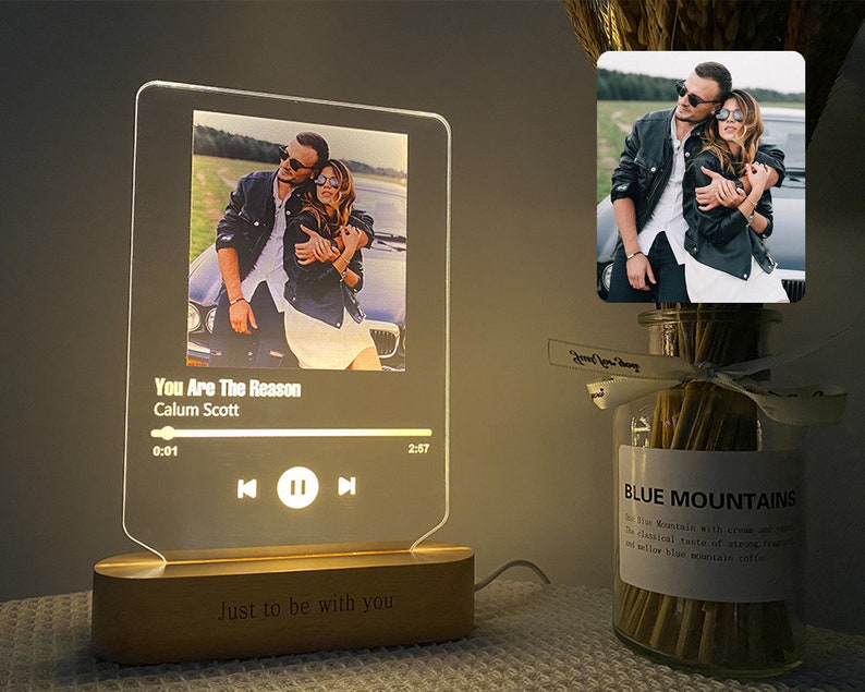 May include: A clear acrylic music player with a photo of a couple in the background. The player has a song title, artist name, and play controls. The base of the player is wood and has the text "Just to be with you".