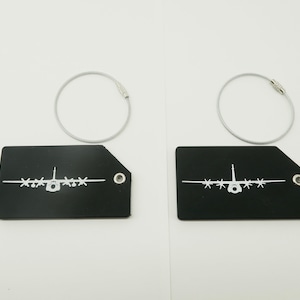 May include: Two black luggage tags with a white airplane design and silver key rings. The tags have a rectangular shape with a cut-off corner and a metal grommet for the ring.