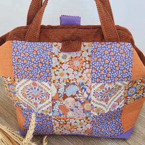 Peut inclure: Un sac fourre-tout avec un motif patchwork composé de carrés de tissu à fleurs et à motifs dans des tons de violet, orange et crème. Le sac possède des anses en velours côtelé marron et une bordure supérieure en velours côtelé marron.