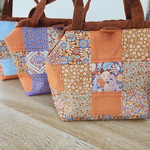 Peut inclure: Trois sacs fourre-tout patchwork avec des poignées et des dessus en velours côtelé marron. Les sacs présentent un mélange de carrés de tissu floral et orange uni. Le fond est un grain de bois clair.