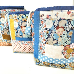 Peut inclure: Trois pochettes à cordon avec un design en patchwork composé de motifs floraux, de pois et d'une illustration centrale d'une personne aux cheveux roux. Les sacs ont une bordure supérieure bleu foncé, un cordon blanc et un embout à pois bleu et blanc.