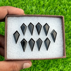 May include: A box of ten black gemstone cabochons in a kite shape. The gemstones are displayed in a white foam insert.