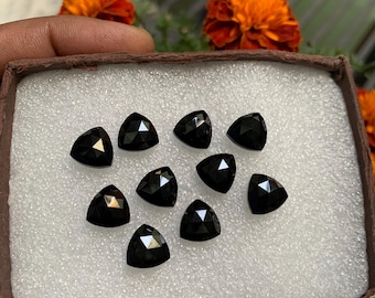 May include: A box of ten black gemstone cabochons in a triangular shape. The gemstones are displayed on a white foam background.