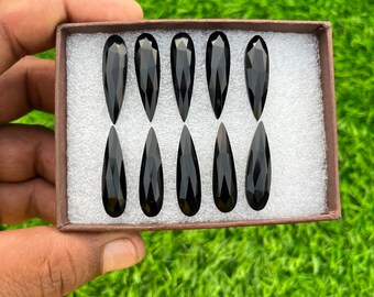 May include: Eight black pear-shaped gemstones in a white foam-lined box. The box is brown and has a white interior.