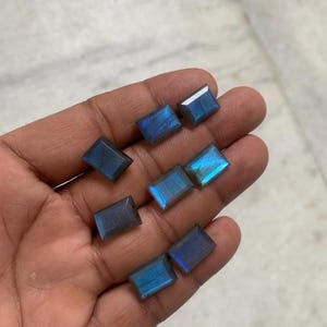 May include: A collection of eight blue labradorite gemstones, cut into rectangular shapes, with iridescent flashes of color.