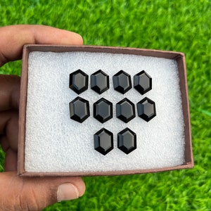 May include: A box containing twelve black octagon-shaped gemstones. The gemstones are arranged in a heart shape.