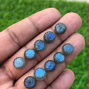 Könnte beinhalten: Zehn irisierende blaue Labradorit-Cabochons mit einem geschnitzten Augenmotiv. Jeder Cabochon hat einen Durchmesser von etwa 10 mm und einen gewellten Rand.