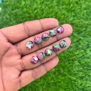 May include: A collection of eight round, green, pink, and white gemstone cabochons. The cabochons are smooth and polished.