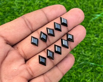 May include: A collection of ten black square-shaped gemstones, likely onyx, displayed on a hand. The gemstones are faceted and have a shiny, polished finish.