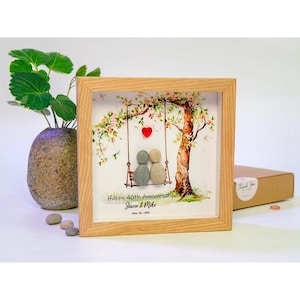 Könnte beinhalten: Ein gerahmtes Kunstwerk mit einem hellen Holzrahmen. Das Kunstwerk zeigt einen Baum mit einer Schaukel, einem roten Herzen und zwei Kieselsteinfiguren. Der Text lautet "Happy 40th Anniversary Stacie & Mike May 26, 1984."