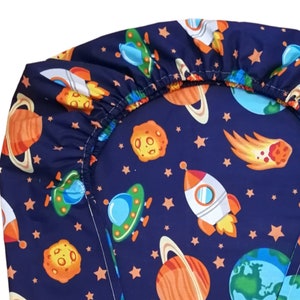 May include: A blue fitted sheet with a space-themed print. The print features planets, stars, rockets, and UFOs in orange, yellow, green, and white.