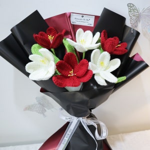 This is a black themed knitted tulip bouquet containing 3 red, 3 white knitted tulips, green cotton thread wrapped around wire to make rhizomes with a leaf on each rhizome, wrapping paper is black. The ribbon is white.