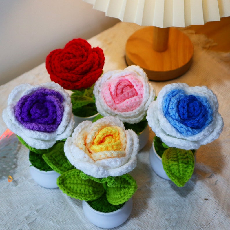 This is a knitted potted plant featuring knitted roses with a white frosted plastic base and knitted flowers in red, pink and white, blue, yellow and purple colors