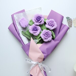 This is a purple themed knitted rose bouquet containing 4 purple knitted roses, 1 purple knitted tulip, green cotton thread wrapped around wire to create a rhizome, the wrapping paper is purple and the ribbon is white!