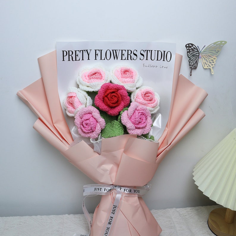 This is a pink themed knitted rose bouquet. Contains 1 red, 2 light pink and 4 white-pink knitted roses. Green cotton thread is wrapped around wire to create a rhizome with three leaves on the rhizome. Wrapping paper is pink and ribbon is white