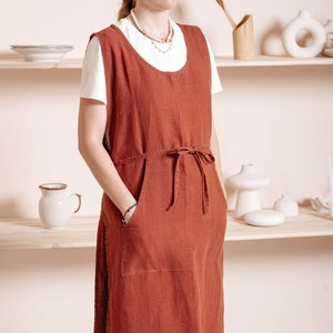 May include: A long, rust-colored linen apron with a single large pocket and a tie at the waist.