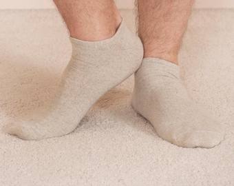 Può includere: Un paio di calzini beige da caviglia in tessuto morbido e testurizzato. I calzini sono indossati sui piedi di una persona.