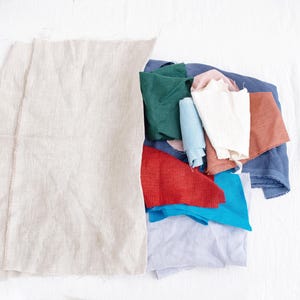 May include: A collection of fabric scraps in various colors, including red, blue, green, white, and brown. The fabric scraps are arranged in a pile on a white surface.