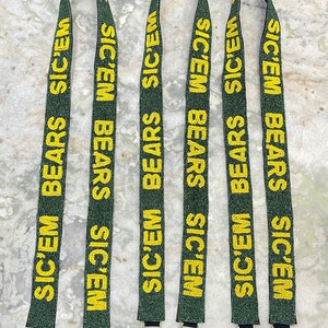Puede incluir: Cinco cordones de cuentas verdes y doradas con el texto "SIC'EM BEARS" repetido en cada cord&oacute;n. Cada cord&oacute;n tiene un cierre plateado.