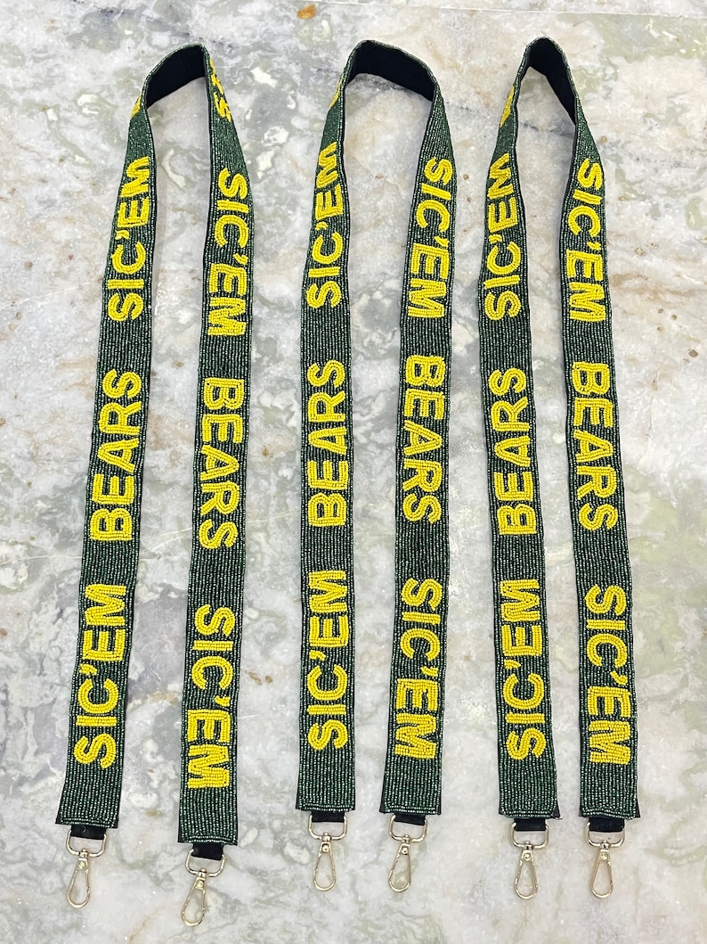 Puede incluir: Cinco cordones de cuentas verdes y doradas con el texto "SIC'EM BEARS" repetido en cada cord&oacute;n. Cada cord&oacute;n tiene un cierre plateado.