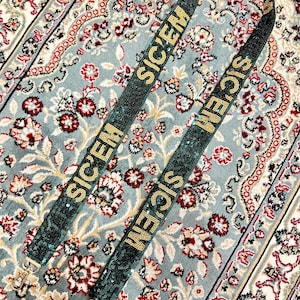 Puede incluir: Dos correas de lentejuelas verdes y doradas con la palabra "SICEM" repetida en cada correa. Las correas est&aacute;n sobre una alfombra estampada.
