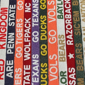 May include: A close-up of a beaded garland with various college team names and logos. The garland is made of white beads with colorful lettering. The names include "Kingdom", "Penn State", "Tigers", "Wolfpack", "Texans", "Ducks", "Vols", "Bears", "Razorbacks", "Sic'em Bears", and "Antonio".