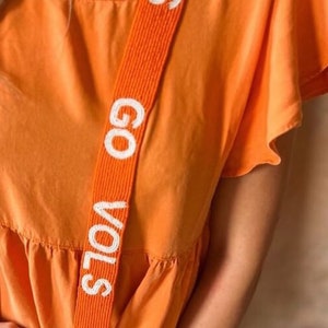 May include: Orange dress with a white beaded strap that says "GO VOLS".