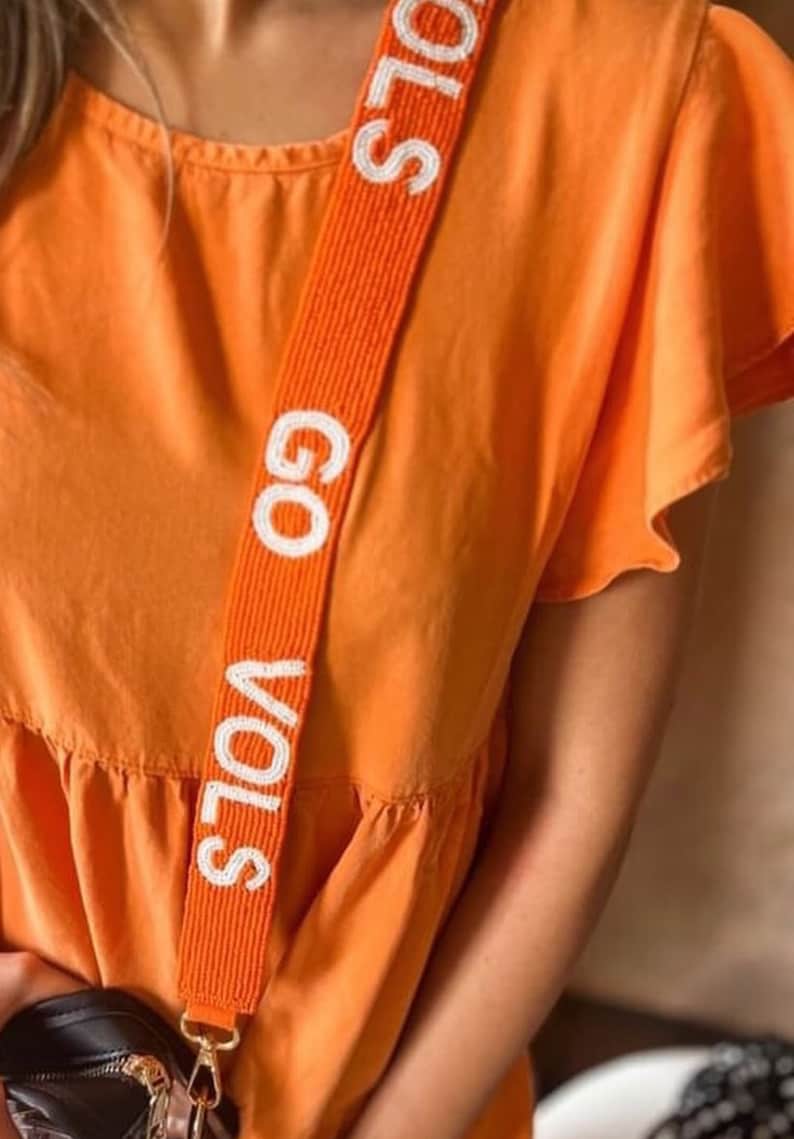 May include: Orange dress with a white beaded strap that says "GO VOLS".