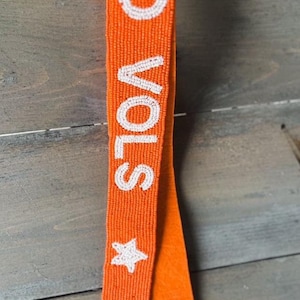 May include: Orange beaded bag strap with white beads spelling "GO VOLS" and a white star. The strap has two gold clasps.