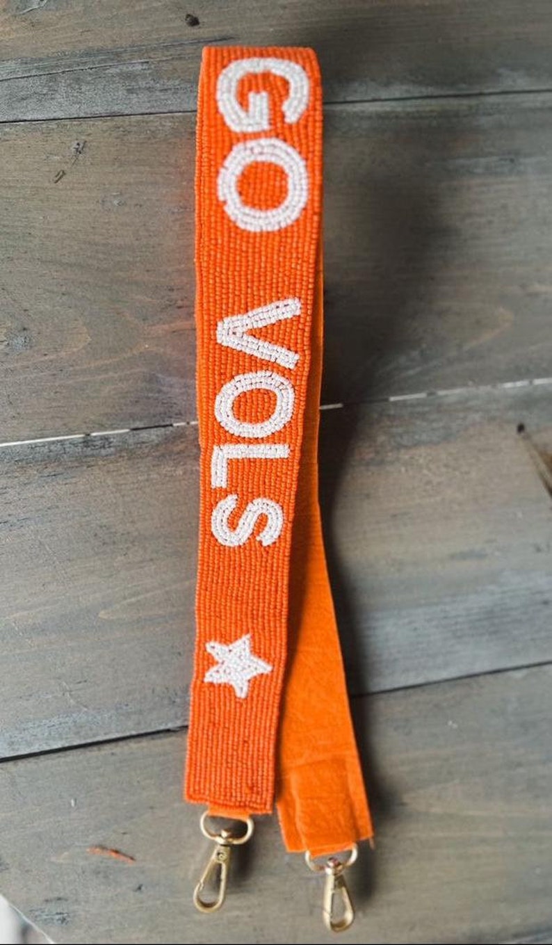 May include: Orange beaded bag strap with white beads spelling "GO VOLS" and a white star. The strap has two gold clasps.