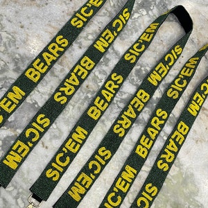 Puede incluir: Cinco cordones de cuentas verdes y doradas con el texto "SIC'EM BEARS" repetido en cada uno. Los cordones tienen cierres de metal dorado.