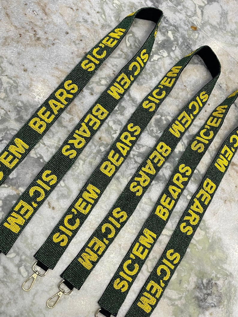 Puede incluir: Cinco cordones de cuentas verdes y doradas con el texto "SIC'EM BEARS" repetido en cada uno. Los cordones tienen cierres de metal dorado.