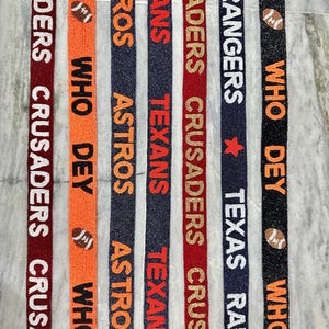 May include: Six different types of colorful beaded trim with various team names and logos. The trim features the names "Crusaders", "Texans", "Astros", "Rangers", and "Who Dey".