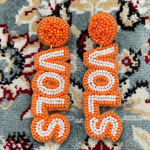 May include: A pair of orange and white beaded earrings that spell out the word "LOVE".