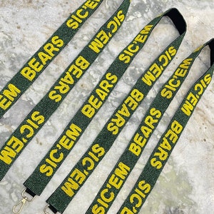 Puede incluir: Cinco correas de cuentas verdes y doradas con las palabras "SIC'EM BEARS" repetidas en cada correa. Cada correa tiene un cierre de metal dorado.