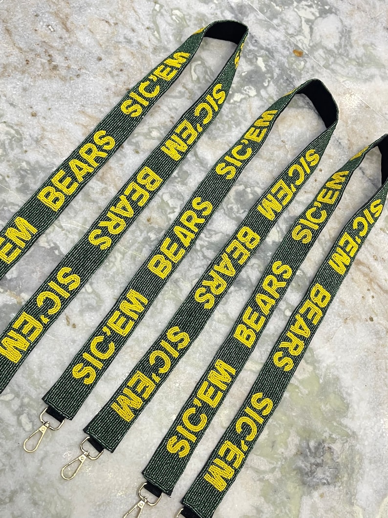 Puede incluir: Cinco correas de cuentas verdes y doradas con las palabras "SIC'EM BEARS" repetidas en cada correa. Cada correa tiene un cierre de metal dorado.