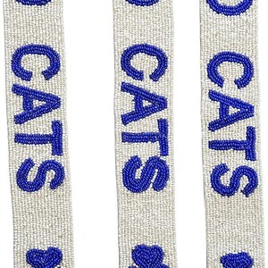 K&ouml;nnte beinhalten: Drei wei&szlig;e Perlenb&auml;nder mit den Worten "GO CATS" in blauen Perlen. Jedes Band hat unten eine blaue Perlen-Pfotenabdruck.