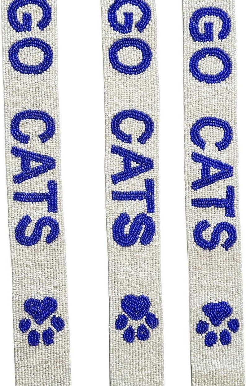 K&ouml;nnte beinhalten: Drei wei&szlig;e Perlenb&auml;nder mit den Worten "GO CATS" in blauen Perlen. Jedes Band hat unten eine blaue Perlen-Pfotenabdruck.