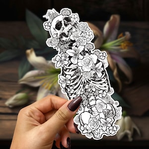 May include: Black and white illustration of a human skeleton with flowers growing from its ribcage and skull. The flowers are detailed and intricate, with delicate petals and stems.