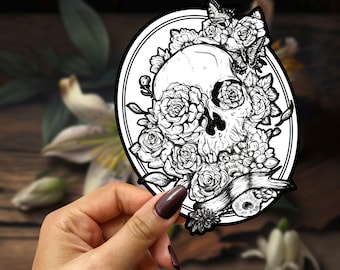 May include: Black and white illustration of a skull with flowers and butterflies. The skull is surrounded by roses and other floral elements. The image is in a circular frame.