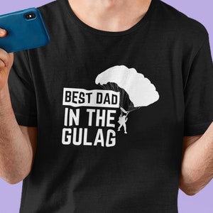 May include: A black t-shirt with a white graphic of a person parachuting from a cloud with the text "BEST DAD IN THE GULAG".