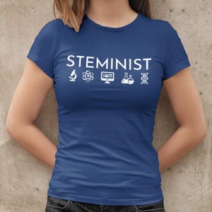 May include: A royal blue t-shirt with the word "STEMINIST" printed in white. The word is accompanied by five white icons: a microscope, an atom, a computer monitor, a beaker, and a DNA double helix.