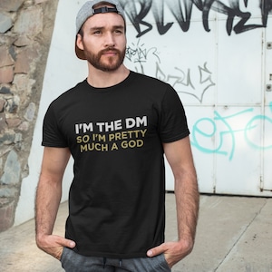 May include: A black t-shirt with the text "I'm the DM so I'm pretty much a god" in gold lettering.