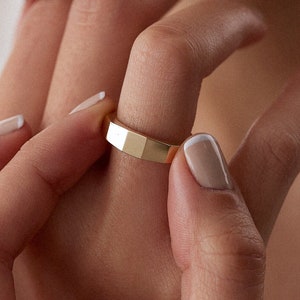 Könnte beinhalten: Ein goldener Bandring mit geometrischem, facettiertem Design. Der Ring wird an einem Finger getragen.