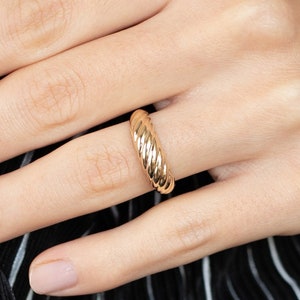 May include: A gold-toned ring with a textured, rope-like design. The ring is worn on a finger.