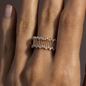 May include: A gold ring with a delicate design featuring a series of vertical bars adorned with small diamonds.