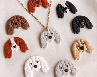 Puede incluir: Un collar de cadena dorada con un colgante en forma de cabeza de perro, rodeado de varios dijes en forma de cabeza de perro en varios colores. Los dijes incluyen tonos de marrón, negro, blanco y beige. Las cabezas de perro tienen detalles.
