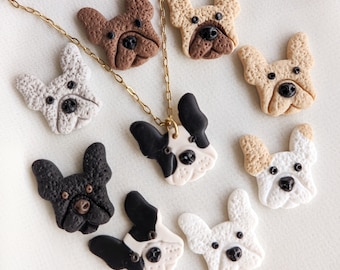 Puede incluir: Una colección de joyas y abalorios con temática de bulldog francés. La imagen presenta un collar de cadena dorada con un colgante y varios abalorios individuales con forma de cabeza de perro en varios colores, incluyendo negro, blanco, marrón y beige.